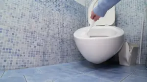 Pulizia di un WC con scopino in un bagno rivestito di piastrelle blu