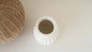 Vaso bianco vuoto accanto a un oggetto in vimini su superficie chiara
