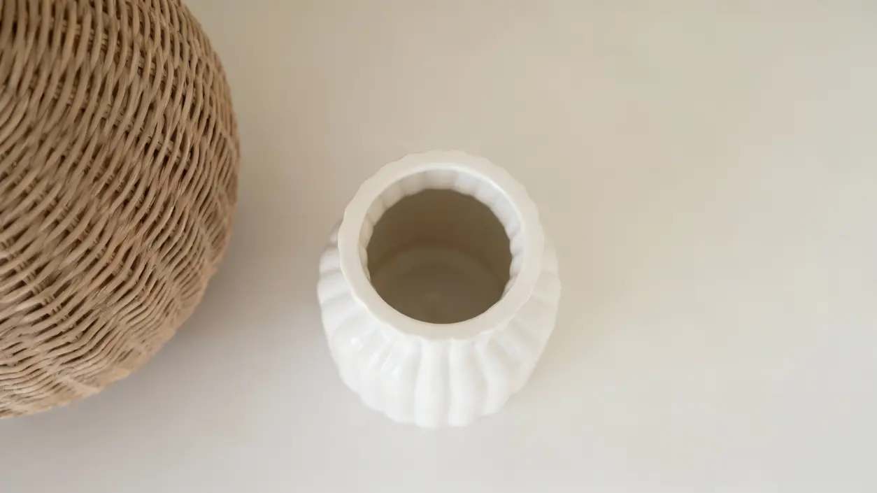 Vaso bianco vuoto accanto a un oggetto in vimini su superficie chiara
