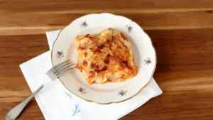 Porzione di lasagna servita su un piatto decorato, appoggiato su tovagliolo bianco