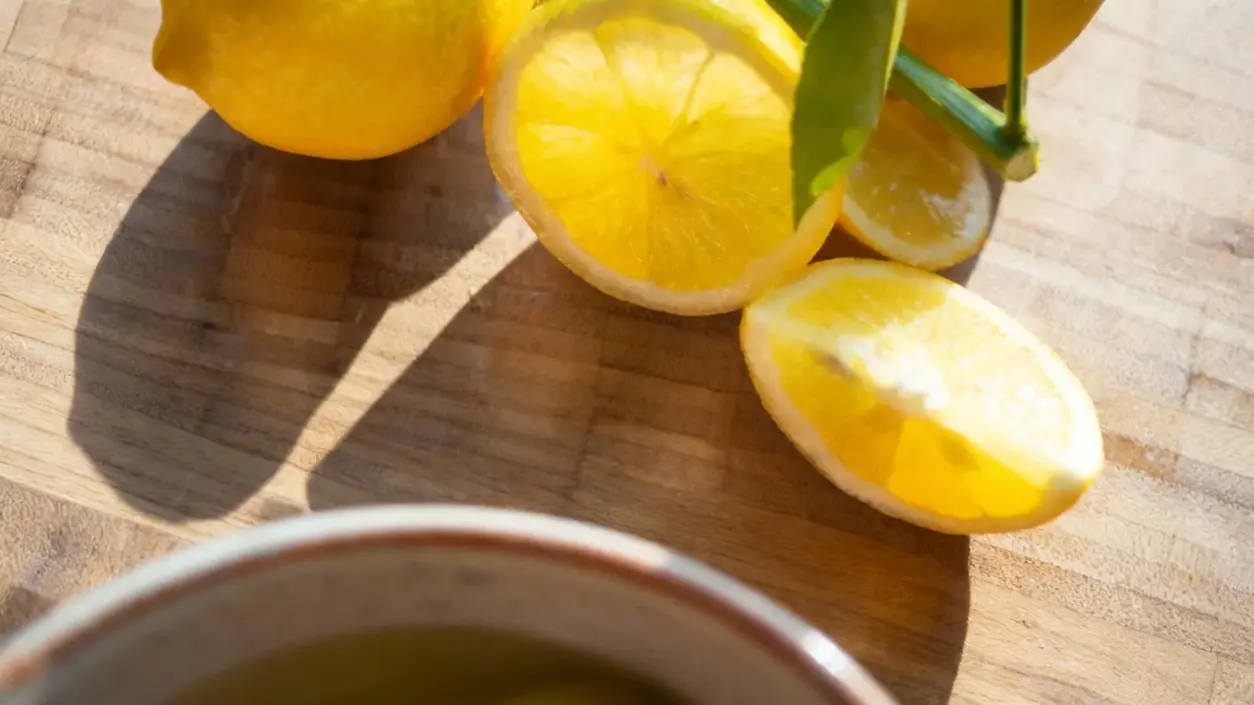 Fette di limone fresco su un tagliere di legno con una tazza parzialmente visibile