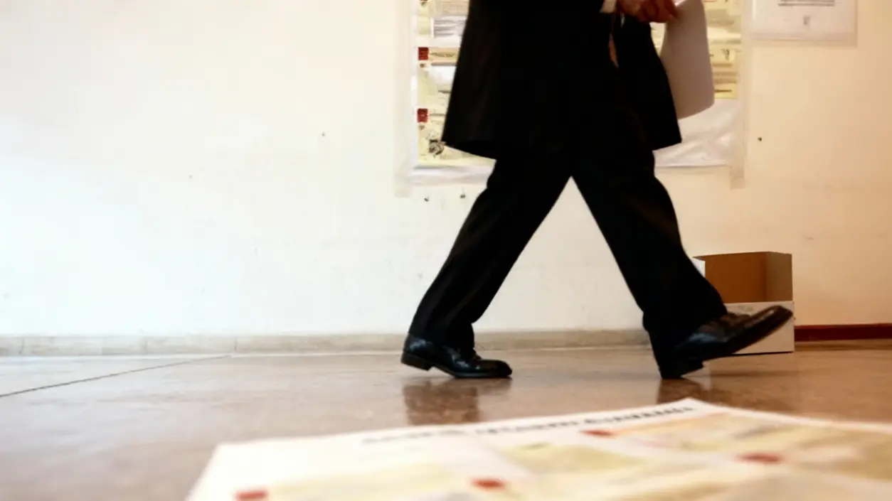 Persona in abito formale cammina lungo un corridoio con documenti in mano