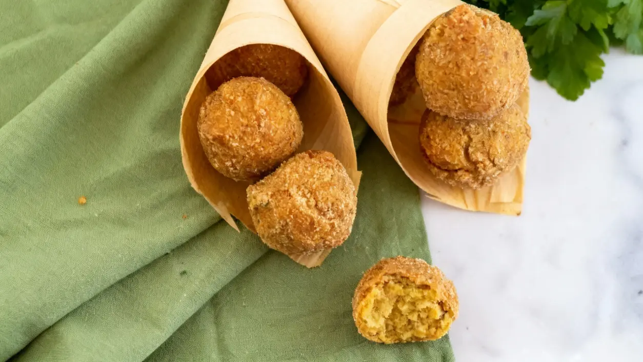 Polpette di ceci croccanti servite in coni di carta su un panno verde