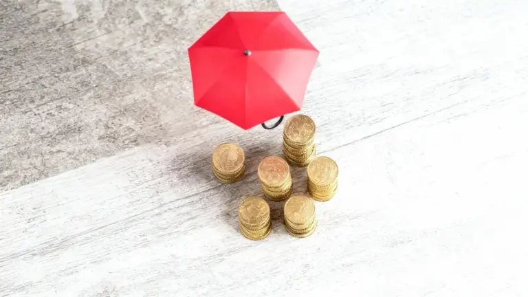 Monete d'oro protette da un piccolo ombrello rosso su superficie chiara