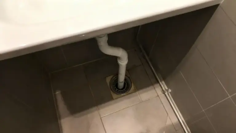 Scarico sotto un lavandino con tubatura visibile in un bagno piastrellato