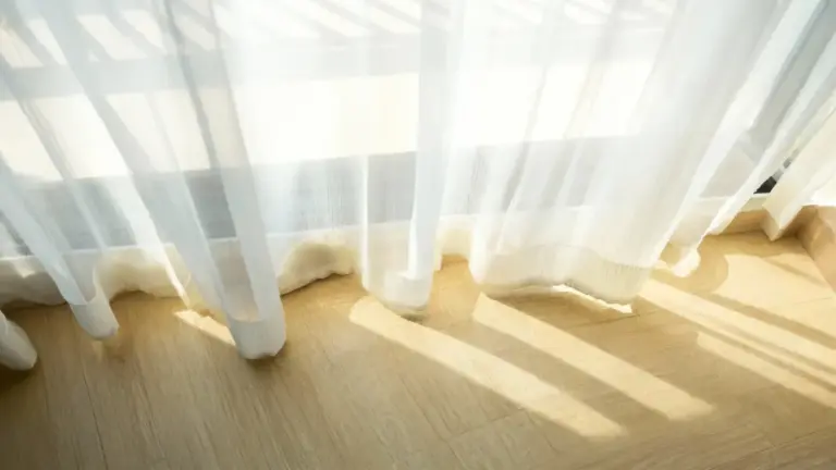 Tende bianche trasparenti illuminate dalla luce del sole su un pavimento chiaro