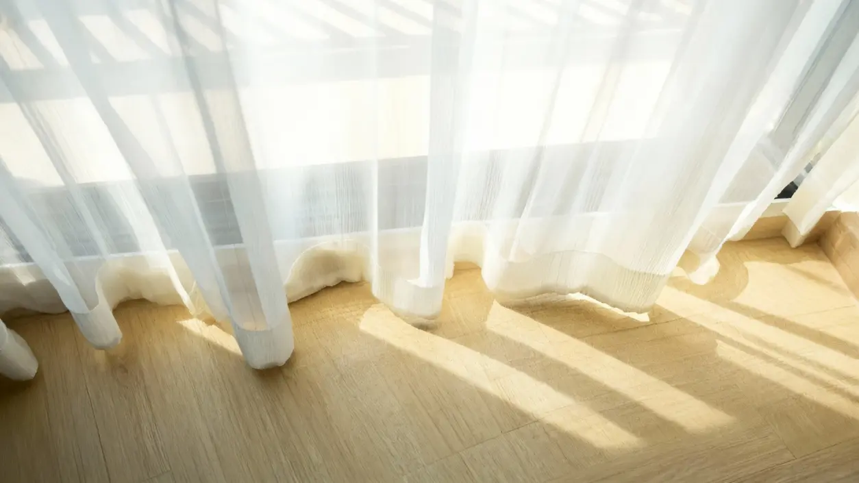 Tende bianche trasparenti illuminate dalla luce del sole su un pavimento chiaro