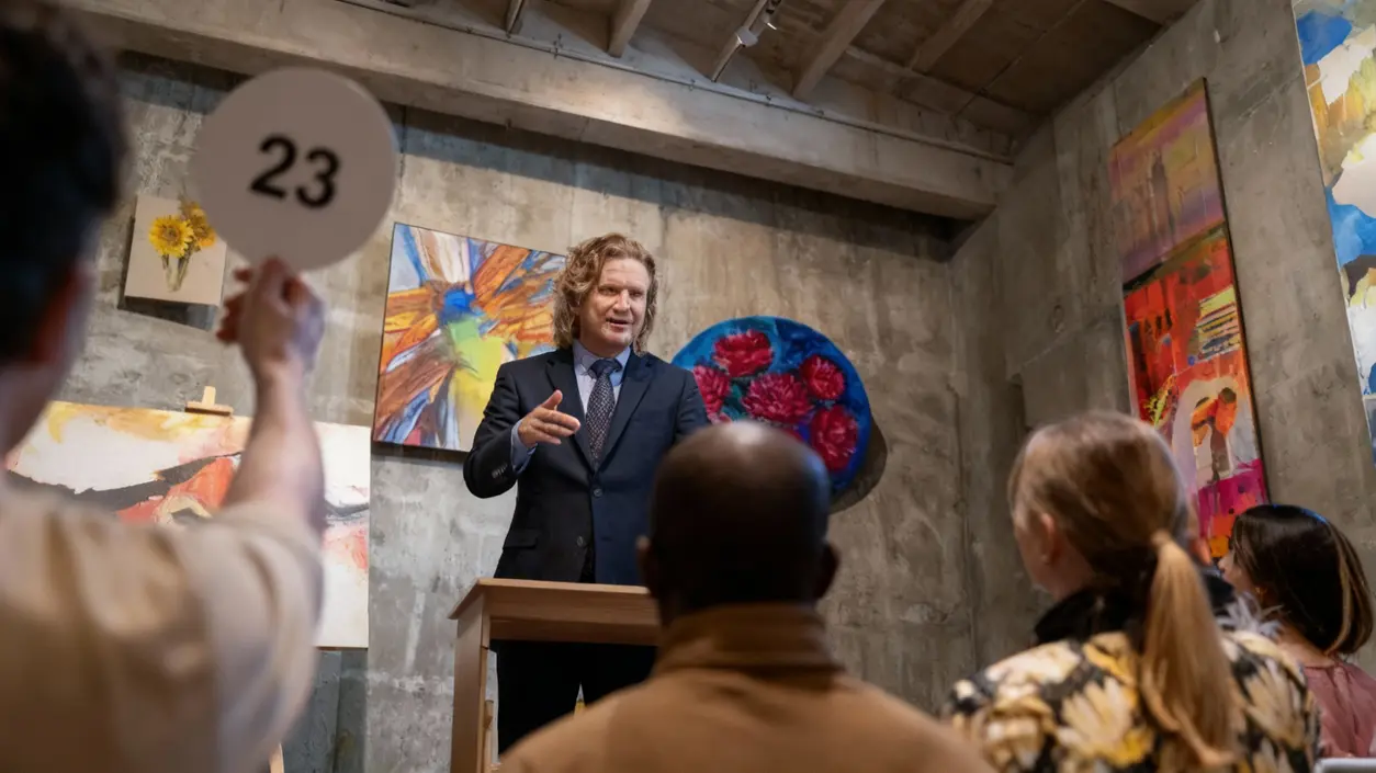 Persona alza una paletta con il numero 23 durante un'asta in una galleria d'arte.