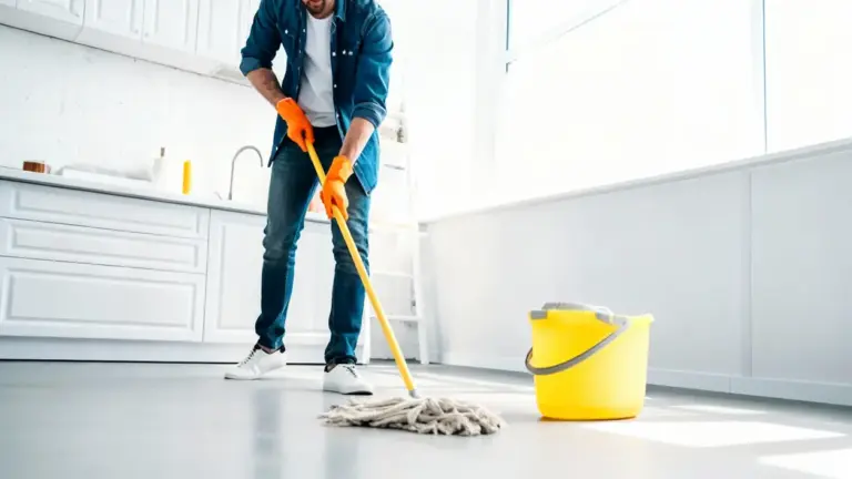 Persona che lava il pavimento con un mocio vicino a un secchio giallo in una cucina luminosa