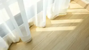 Tende bianche leggere che sfiorano un pavimento in legno chiaro illuminate dal sole