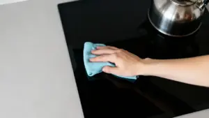 Mano che pulisce un piano cottura con un panno in microfibra azzurro