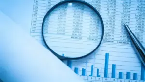 Lente d'ingrandimento su un foglio con tabelle numeriche e grafici finanziari