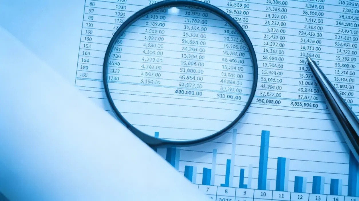 Lente d'ingrandimento su un foglio con tabelle numeriche e grafici finanziari