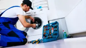 Tecnico controlla l'interno di una lavatrice con attrezzi sul pavimento