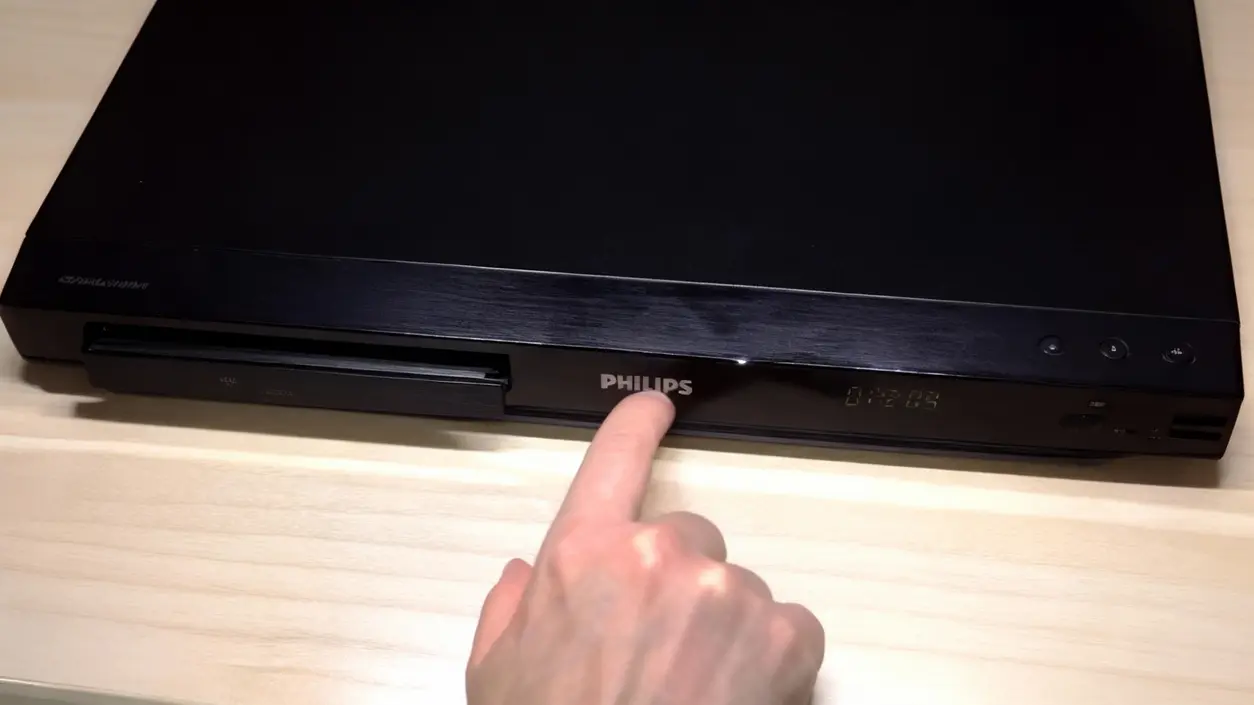 Una mano preme il tasto di apertura su un lettore DVD nero su un tavolo di legno chiaro