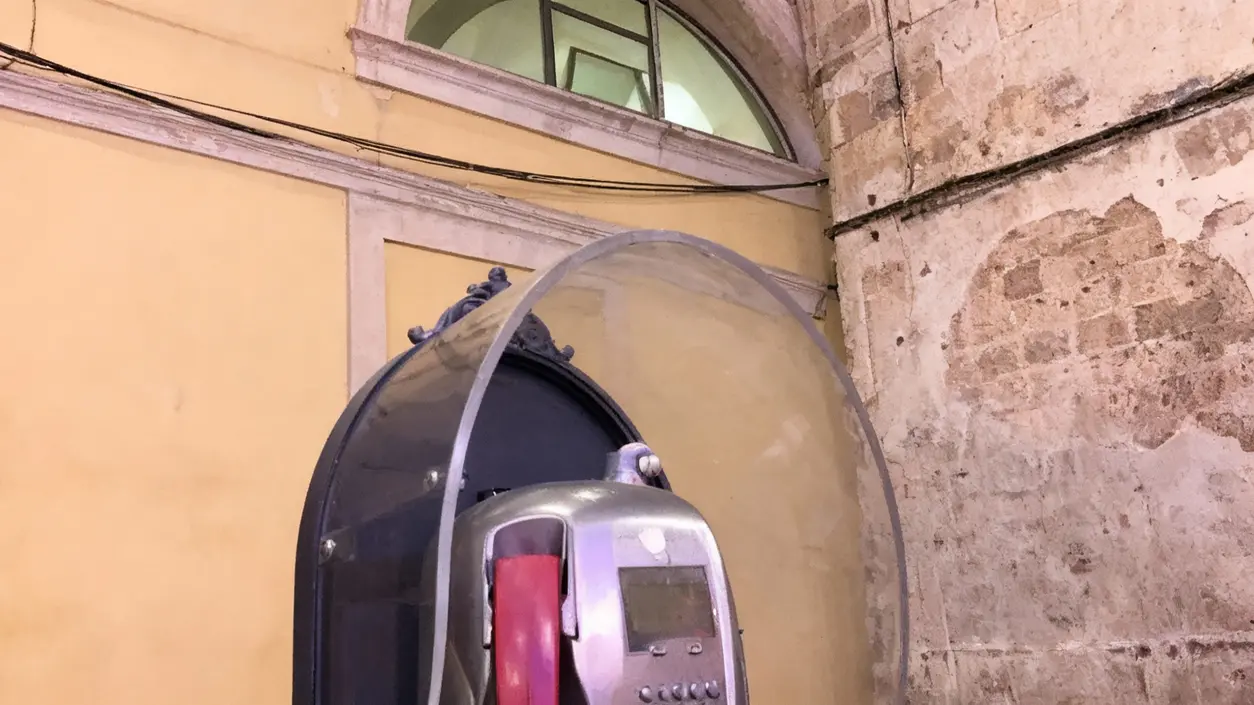 Cabina telefonica con telefono pubblico in un vicolo con muri antichi