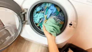 Una mano estrae dei vestiti colorati dalla lavatrice a carica frontale