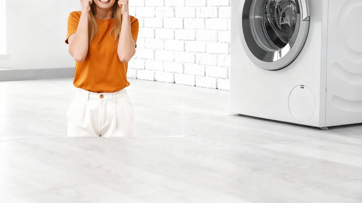 Una persona accanto a una lavatrice in una stanza luminosa, apparentemente frustrata
