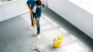 Persona che pulisce il pavimento con un mocio e secchio giallo in una cucina luminosa