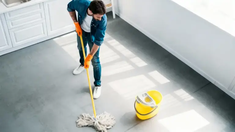 Persona che pulisce il pavimento con un mocio e secchio giallo in una cucina luminosa