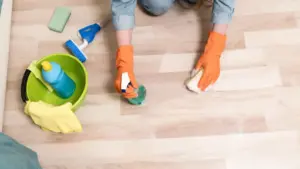 Persona con guanti arancioni pulisce un pavimento chiaro con spugna e spray