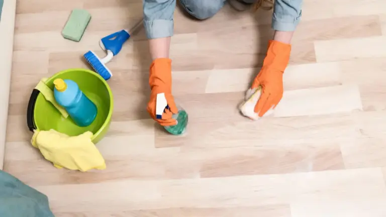 Persona con guanti arancioni pulisce un pavimento chiaro con spugna e spray