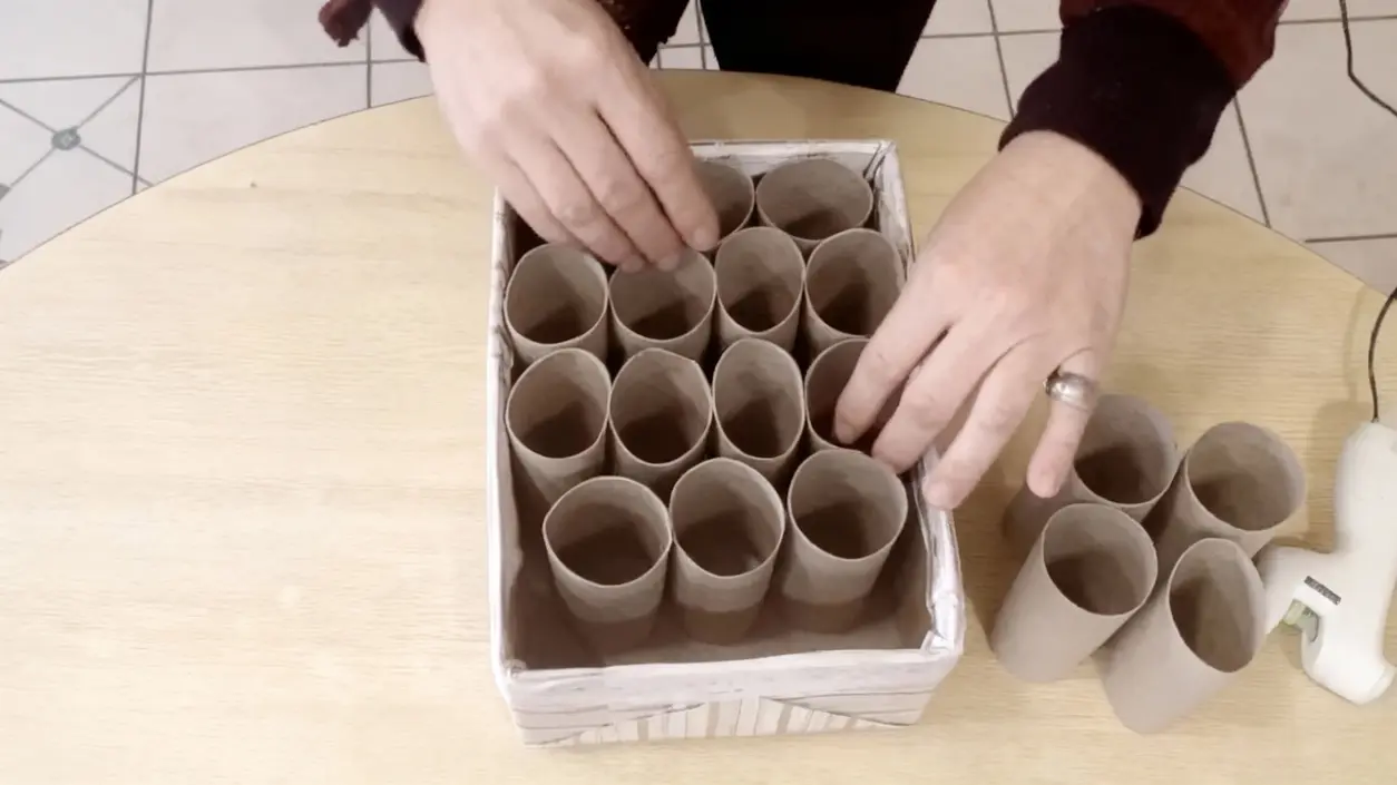 Mani che sistemano rotoli di carta igienica in una scatola per un'organizzazione domestica creativa