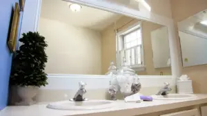 Specchio del bagno pulito sopra un lavabo doppio con decorazioni e contenitori in vetro