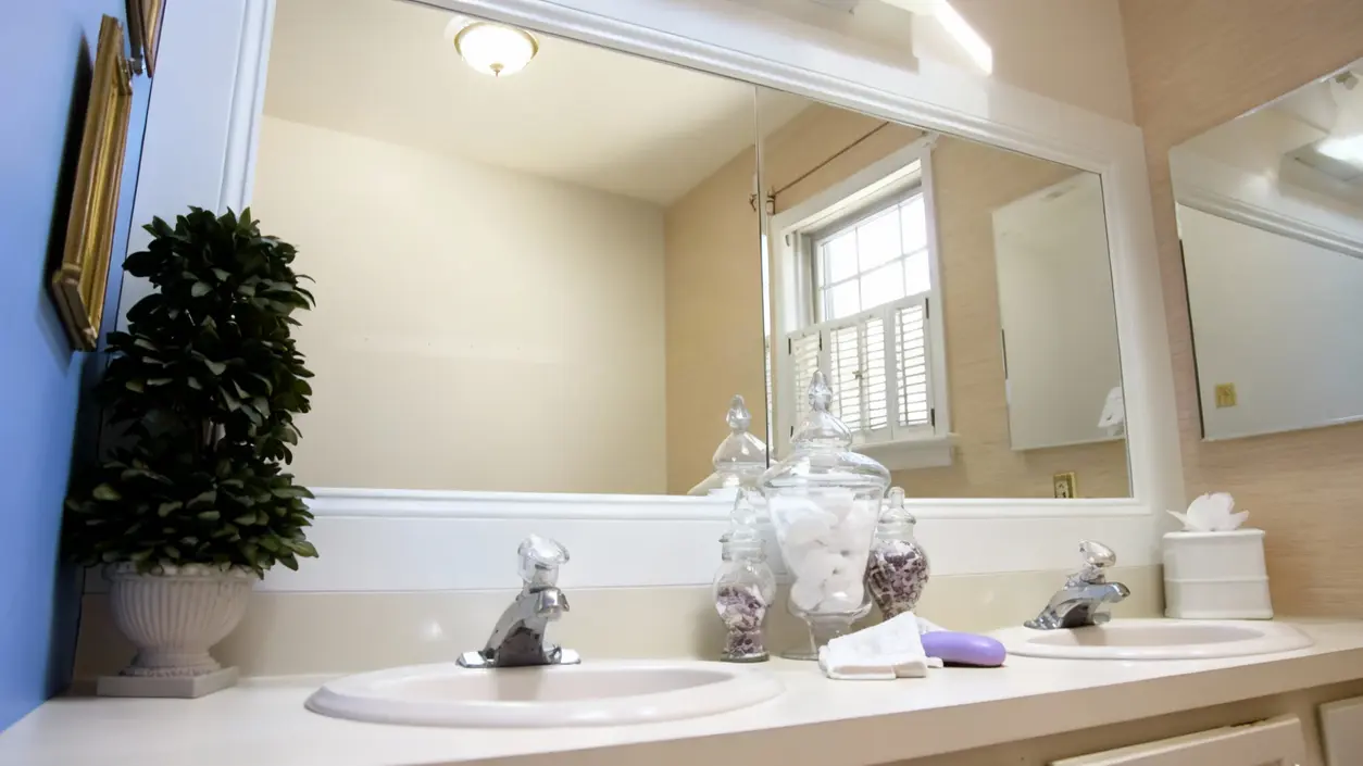 Specchio del bagno pulito sopra un lavabo doppio con decorazioni e contenitori in vetro